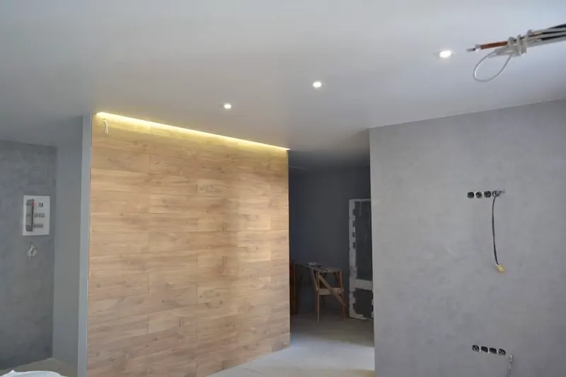 Bad mit großformatigen grauen Platten, Holzoptik-Wand und indirekter Beleuchtung
