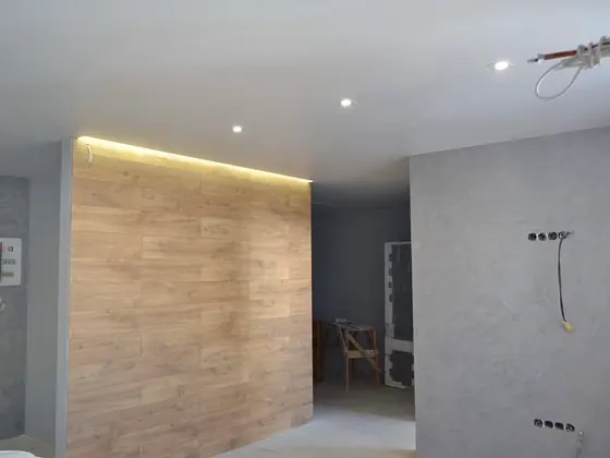 Bad mit großformatigen grauen Platten, Holzoptik-Wand und indirekter Beleuchtung