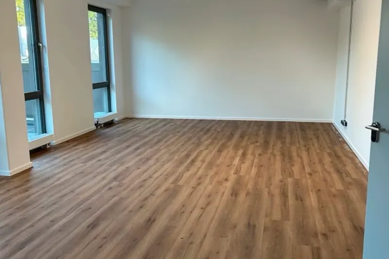 Leerer heller Raum mit neu verlegtem Vinylboden in Eichenoptik und Fensterfront