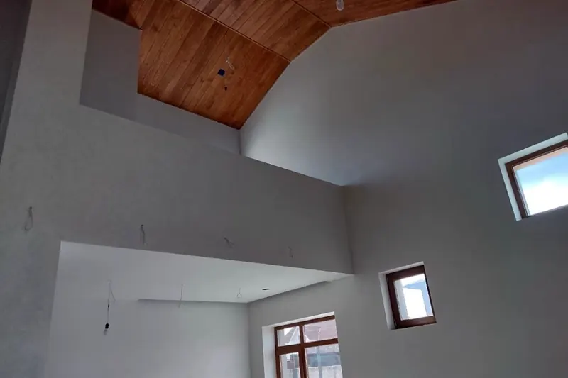 Ausgebauter Dachraum mit dunkler Holzdecke, verputzten Wänden und Dachflächenfenster