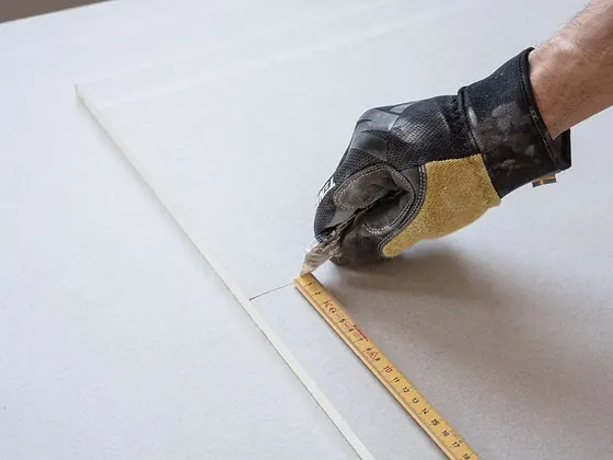Gipskartonplatte wird mit Zollstock angezeichnet und zugeschnitten