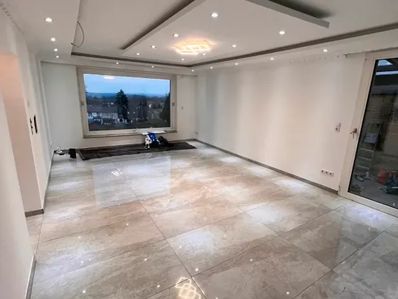 Großer Wohnraum mit glänzendem großformatigem Bodenbelag und abgehängter Decke mit Spots